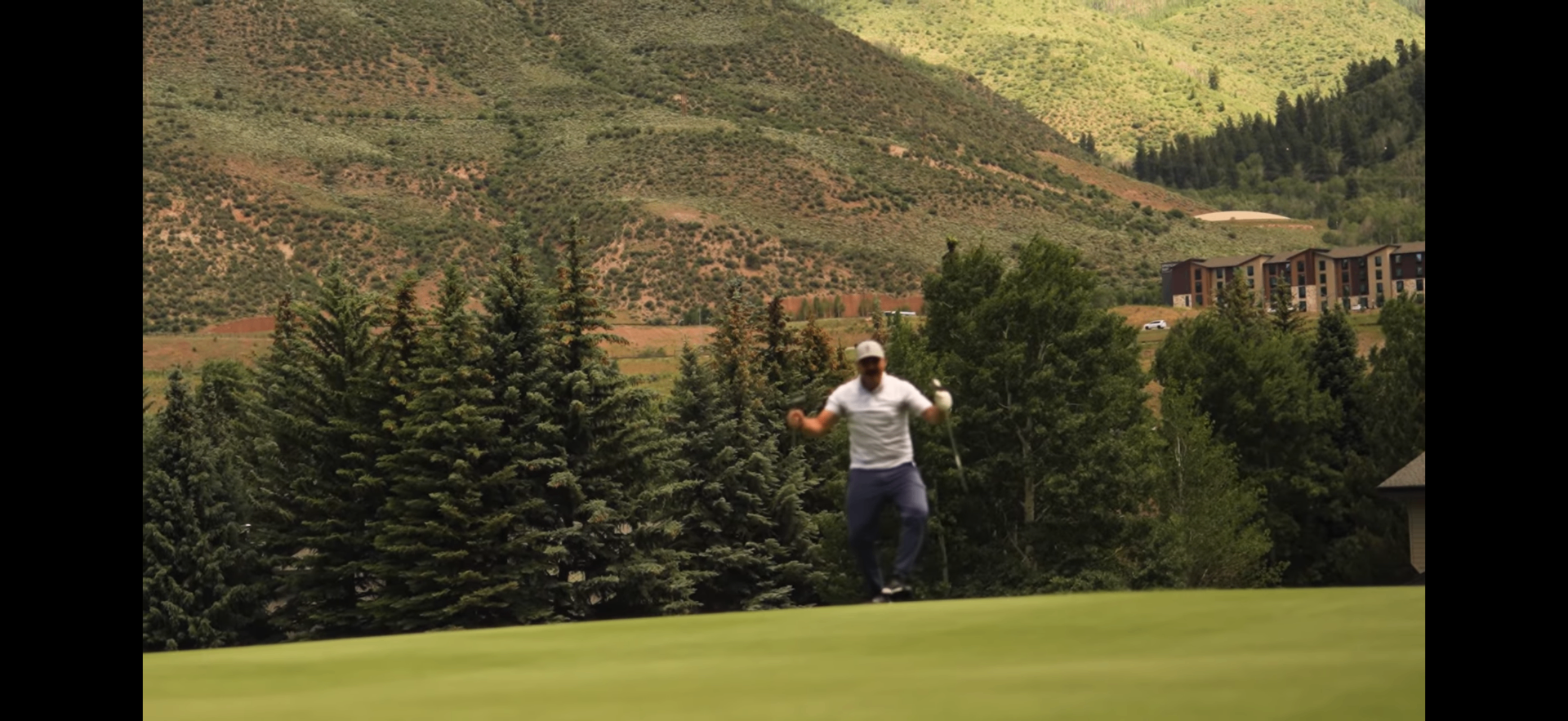 Golfer celebrating a made putt with mountains behind